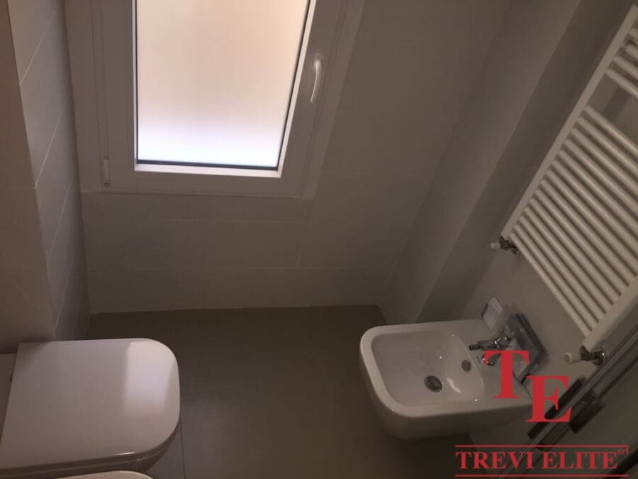 Modern small bathroom with a white bidet, a towel radiator, and a frosted window for natural light. The space is clean, bright, and efficiently designed for comfort and functionality.