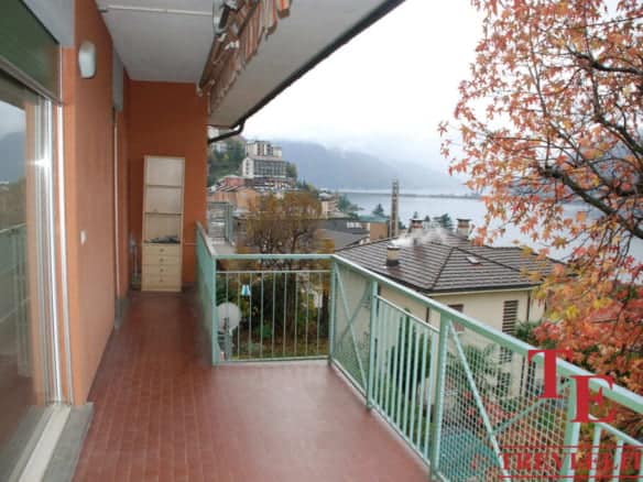 Panoramic view from an Italian lakeside apartment balcony overlooking a misty lake and surrounding houses during autumn.
