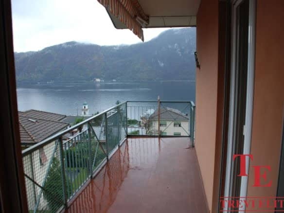 Balcony view of Lake Como with mountains in the background, overlooking a luxurious residential area in Italy with modern architecture and lush greenery, perfect for high-end living and relaxation.