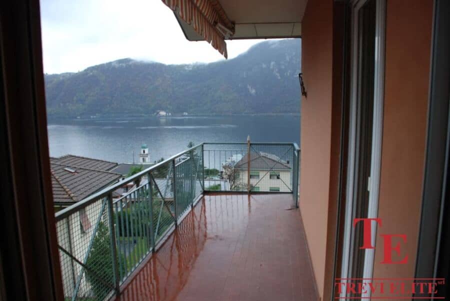 Balcony view of Lake Como with mountains in the background, overlooking a luxurious residential area in Italy with modern architecture and lush greenery, perfect for high-end living and relaxation.