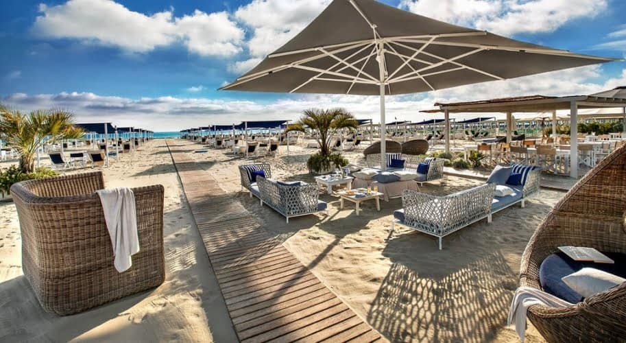 Elegant beachfront lounge area with stylish wicker and fabric seating, sun umbrellas, and sandy pathways, offering a luxurious seaside retreat with breathtaking ocean views. For luxury connoisseurs - Trevi Elite.