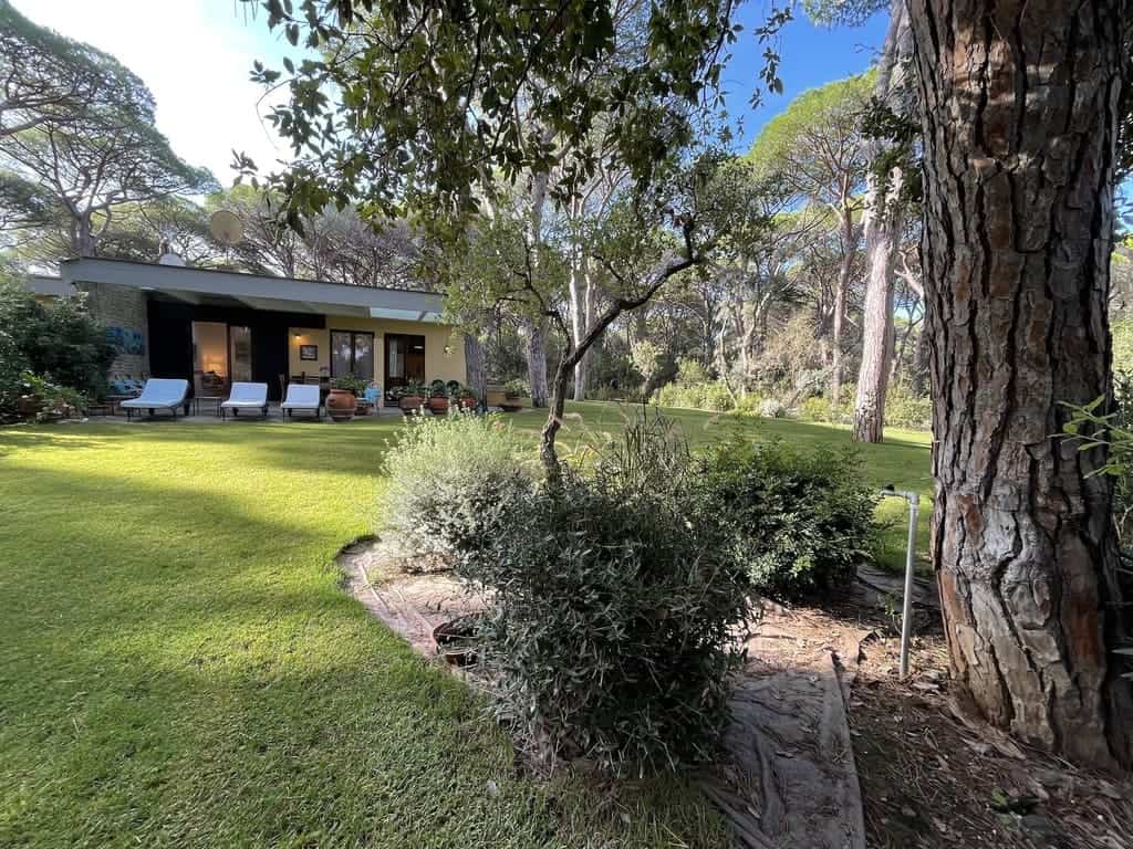 Lush green garden with mature trees and well-maintained lawn, overlooking a modern house with outdoor seating, ideal for relaxing and enjoying nature in Italy.
