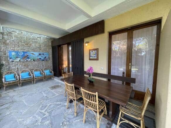 Charming outdoor patio featuring a wooden dining table, rattan chairs, and a stone wall with colourful artwork, ideal for relaxing and entertaining in a luxurious Italian estate.