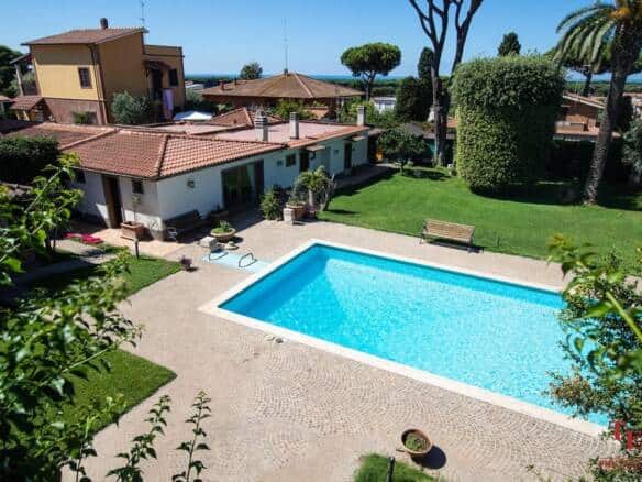 Spacious Italian villa with a private pool, lush garden, and outdoor seating area, situated in a serene residential neighbourhood with scenic views and mature trees.
