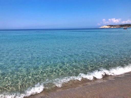 Serene coastal scene with crystal-clear turquoise waters meeting a sandy beach under a bright blue sky in Italy.