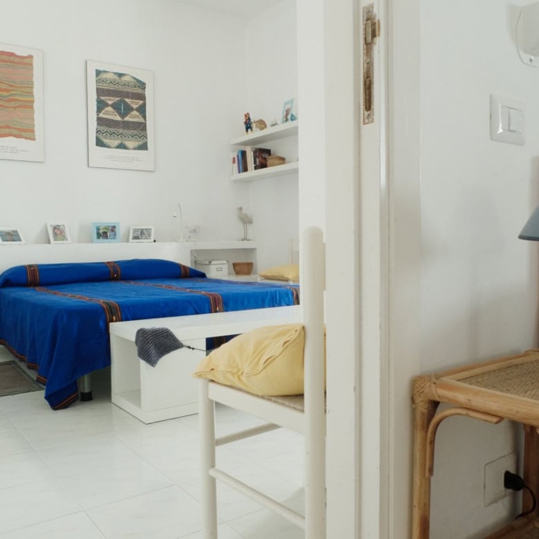 Bright and airy bedroom with a colourful blue bedspread, minimalist white furniture, and vibrant wall art in a modern Italian home. Perfect for a luxurious, comfortable stay in Italy.