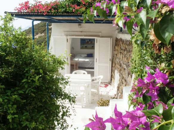 Rose-covered terrace leading to a charming Italian villa with white shutters and lush greenery in a picturesque countryside setting.