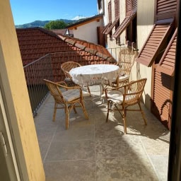 Charming outdoor balcony with wicker furniture and panoramic views of classic Italian rooftops and lush hills, perfect for relaxing and enjoying the Mediterranean climate.