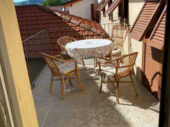 Charming balcony with wicker chairs and a table, overlooking traditional Italian rooftops and scenic hills in the background. Ideal for enjoying outdoor leisure in a luxurious setting.