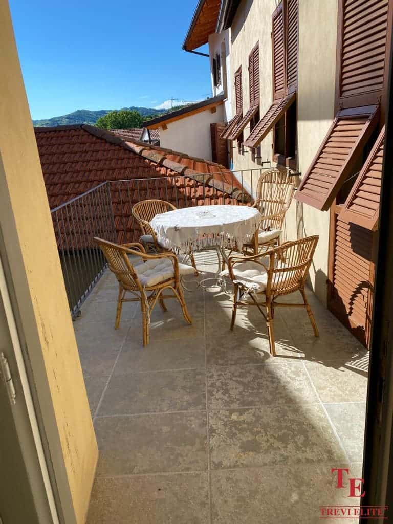 Charming balcony with wicker chairs and a table, overlooking traditional Italian rooftops and scenic hills in the background. Ideal for enjoying outdoor leisure in a luxurious setting.