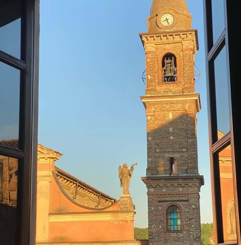 Elegant view of a historic Italian clock tower and statue through a large open window, highlighting classic architecture.