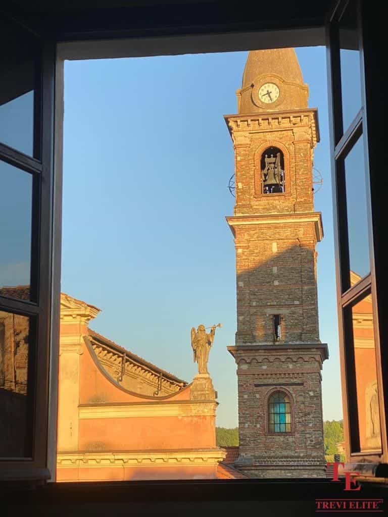Elegant view of a historic Italian clock tower and statue through a large open window, highlighting classic architecture.