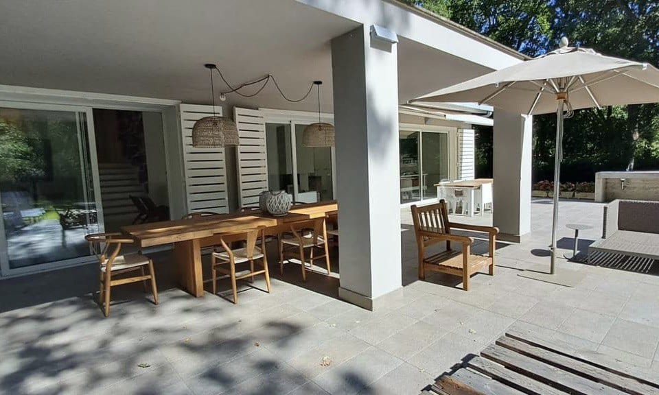Modern outdoor patio with wooden dining table, sun umbrella, and comfortable seating area, ideal for relaxing and entertaining in a contemporary Italian villa.