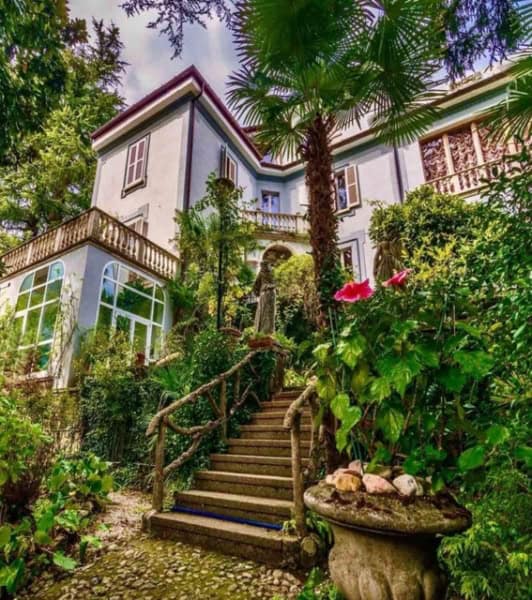 Elegant Italian villa surrounded by lush garden greenery, featuring charming wooden stairs and classic architecture, perfect for luxurious living.