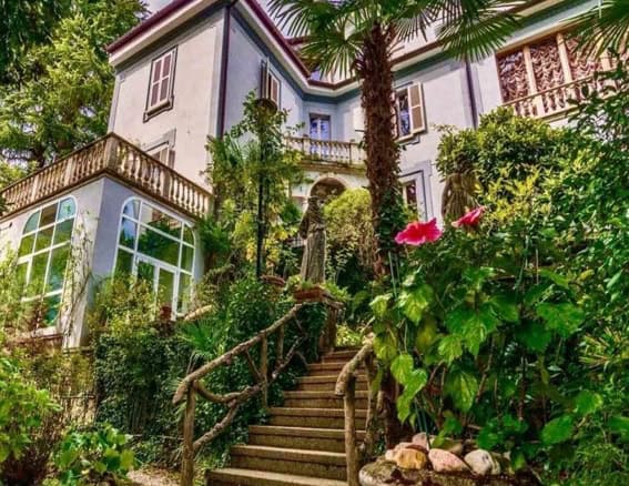 Elegant Italian villa surrounded by lush garden greenery, featuring charming wooden stairs and classic architecture, perfect for luxurious living.