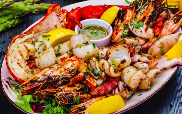 Freshly prepared seafood platter with lobster, shrimp, scallops, and lemon wedges, served with a dipping sauce and garnished with herbs, perfect for seafood lovers.