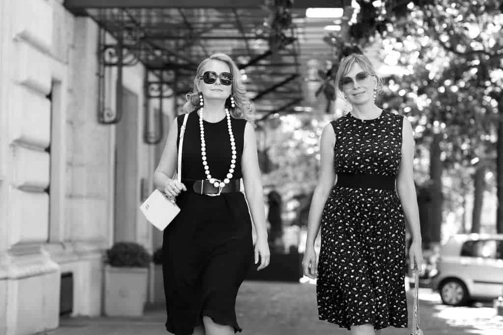 Elegant women walking along a city street in sophisticated summer dresses, reflecting refined fashion and luxury lifestyle.