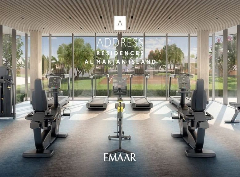 Modern gym with advanced exercise equipment and large floor-to-ceiling windows overlooking lush landscaped gardens at Address Residences, Al Marjan Island.