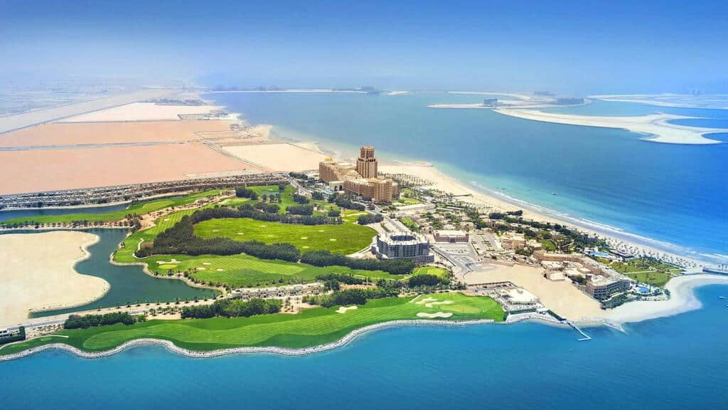 Lush green golf course and resort overlooking the Persian Gulf with luxury buildings and pristine beaches, showcasing high-end Italian real estate opportunities in Dubai’s prime location.