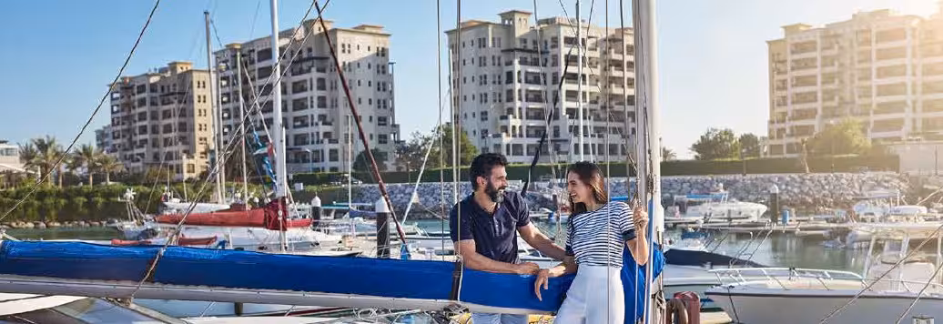 Couple chatting on sailboat at marina with luxury apartments.