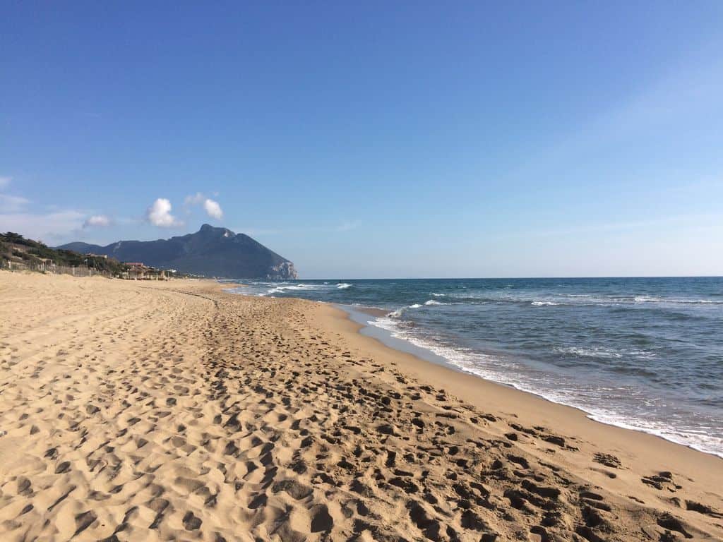 Serene sandy beach with gentle waves and scenic mountain backdrop, perfect for luxury seaside living in Italy. Exceptional coastal property views for discerning connoisseurs. For luxury connoisseurs - Trevi Elite.