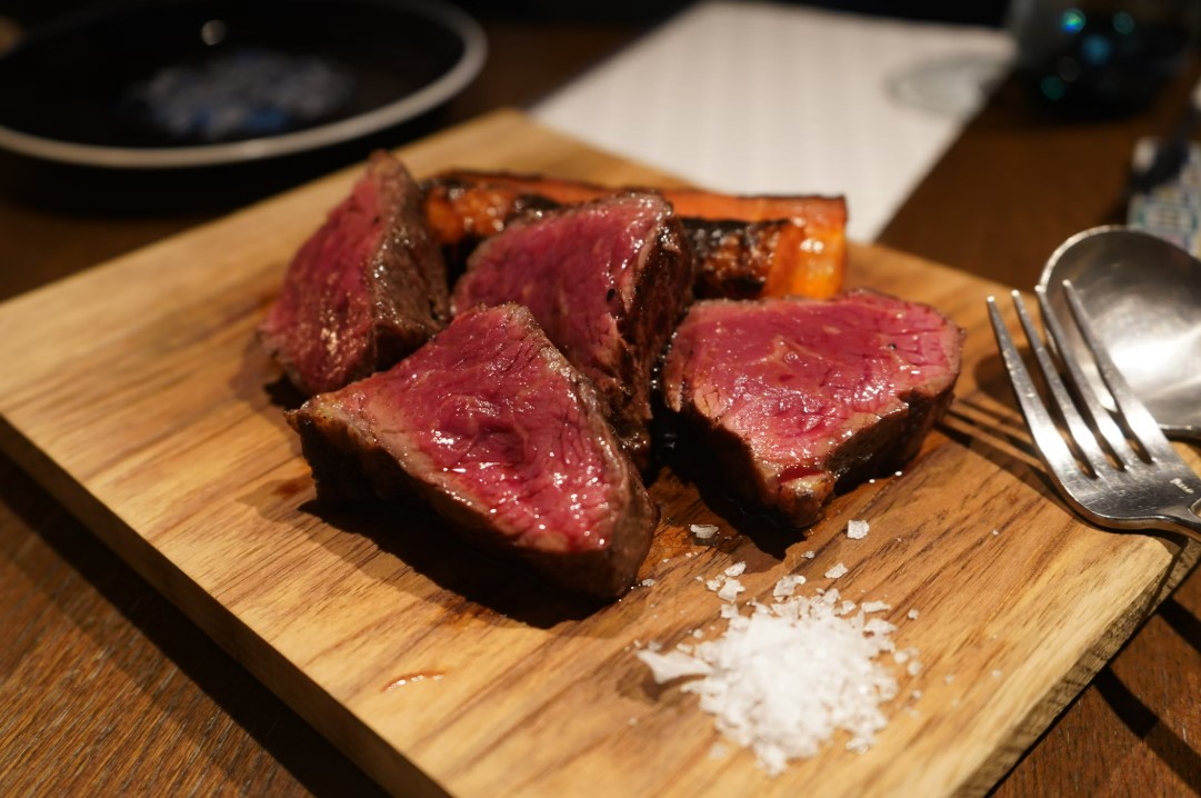 Succulent, perfectly cooked high-quality steak served on a wooden platter with a pinch of sea salt, showcasing fine Italian culinary craftsmanship for luxury connoisseurs - Trevi Elite.