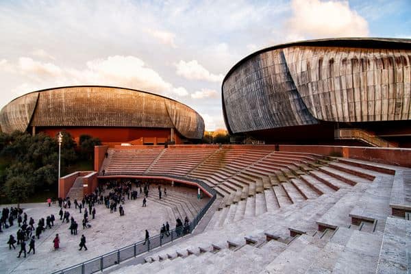 Modern architectural design of the Curva Auditorium in Italy, featuring striking curved structures and an amphitheatre-style outdoor seating area, showcasing exclusive Italian real estate with innovative construction.