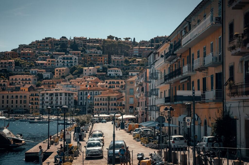 Elegant Italian harbour view with colourful waterfront buildings, boats, and scenic hillside in the background, capturing the charm of exclusive Mediterranean real estate.