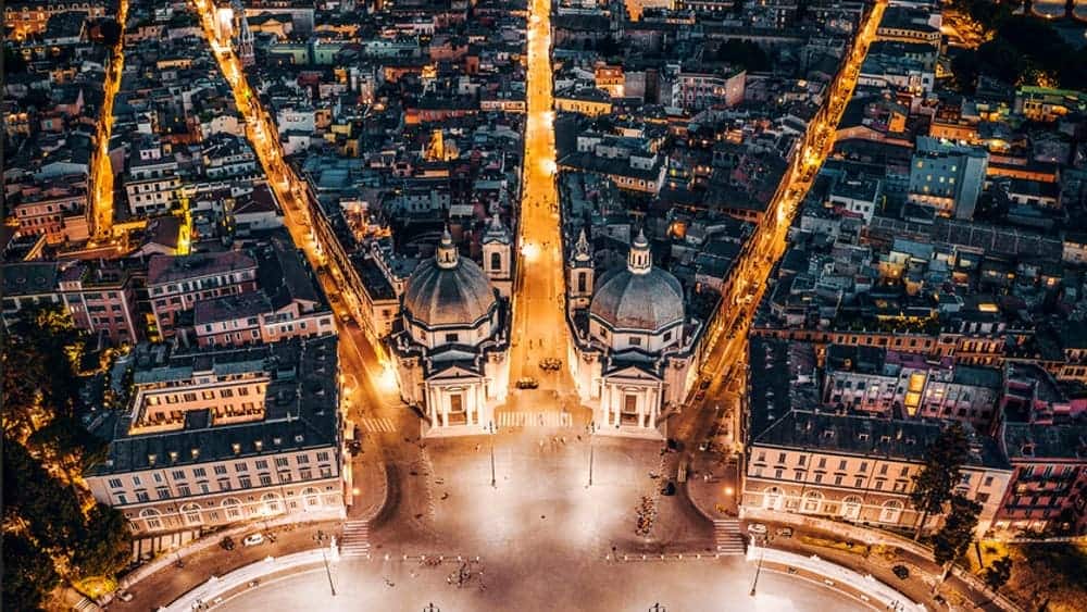 Elegant aerial view of Rome at dusk showcasing illuminated Baroque architecture and bustling city streets, ideal for luxury real estate marketing in Italy.