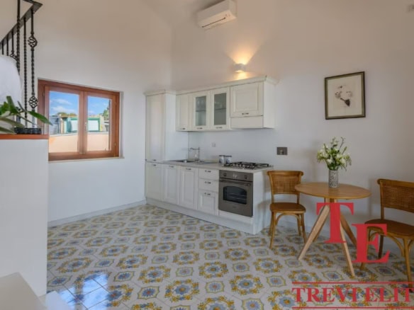 Modern Italian kitchen with white cabinetry, patterned tile flooring, and a cosy dining area with wooden chairs and a small round table. Bright, airy space perfect for Italian living.