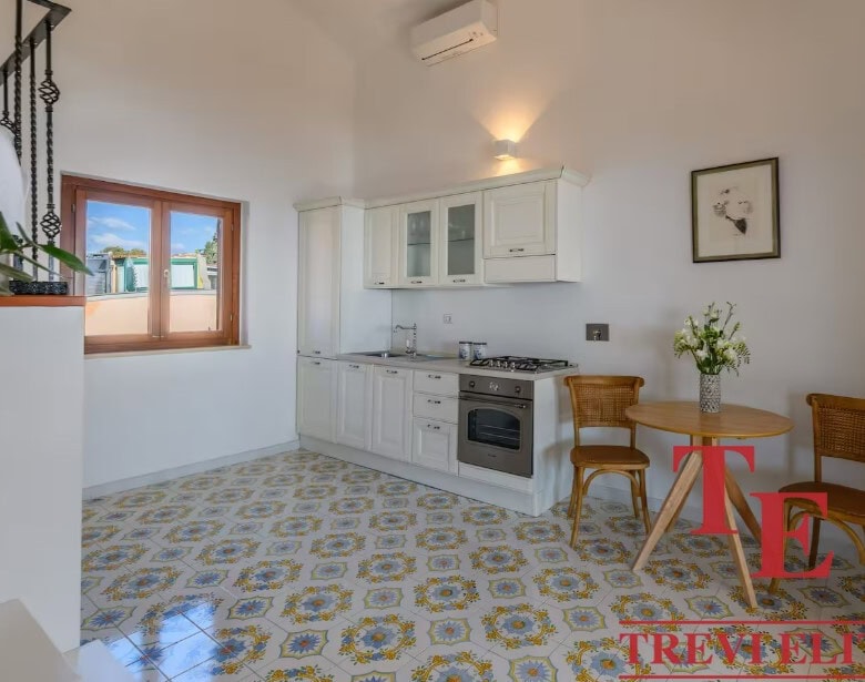 Modern Italian kitchen with white cabinetry, patterned tile flooring, and a cosy dining area with wooden chairs and a small round table. Bright, airy space perfect for Italian living.