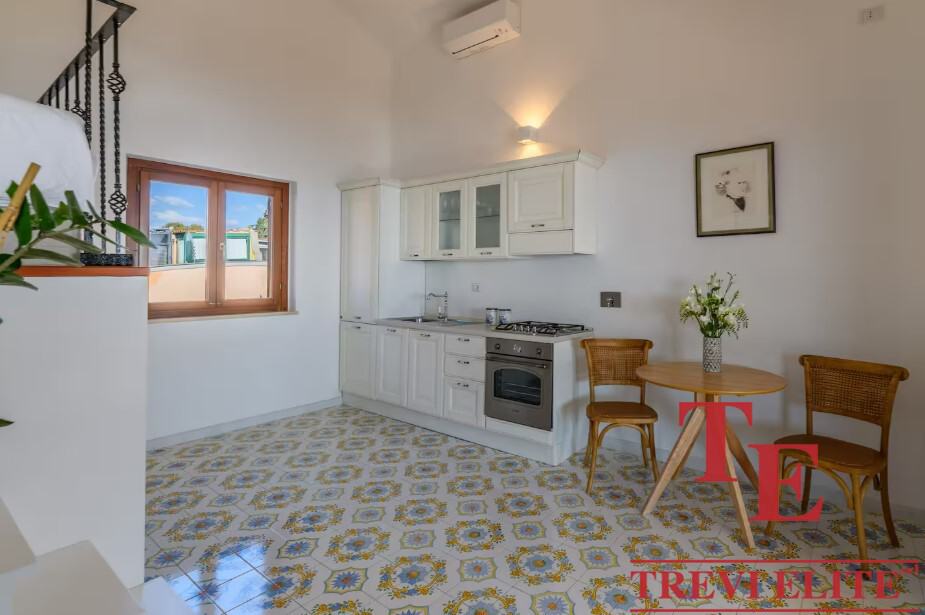 Modern Italian kitchen with white cabinetry, patterned tile flooring, and a cosy dining area with wooden chairs and a small round table. Bright, airy space perfect for Italian living.