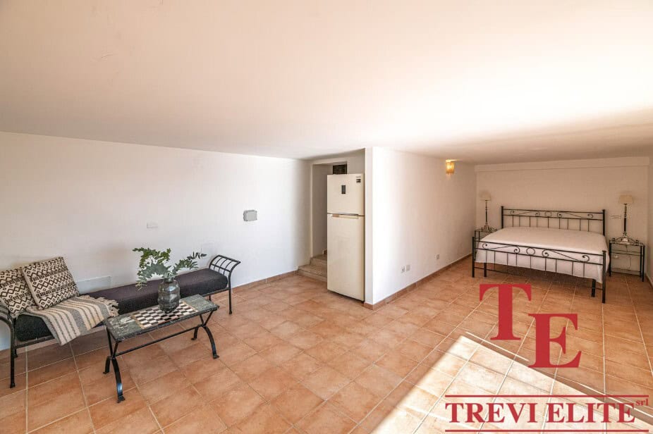 Bright spacious living area with terracotta tiled flooring, minimal decor, and a cosy bedroom corner with a wrought-iron bed frame. Perfect for a comfortable Italian retreat.