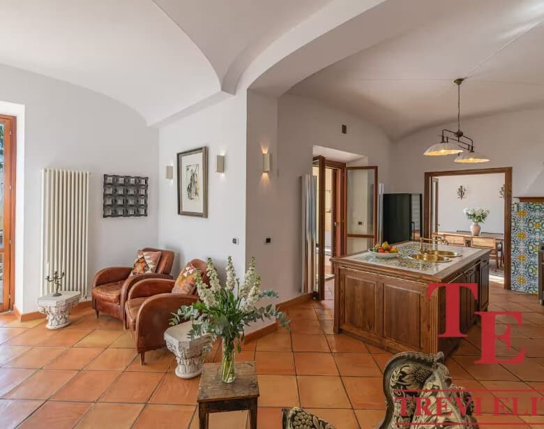 Elegant Italian villa interior with sea view, featuring terracotta floors, cosy seating area, and rustic kitchen with traditional tiles, perfect for luxurious Mediterranean living.
