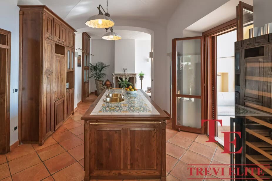 Modern rustic kitchen with wooden cabinetry, tiled countertops, and sunlit courtyard access, ideal for elegant Italian living.