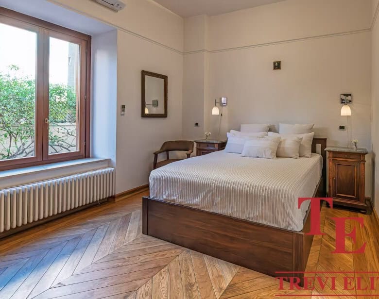 Luxurious Italian bedroom with elegant wooden flooring and classic decor by Trevi Elite. Bright space featuring a large window, cozy bed, and tasteful furnishings, perfect for upscale living.