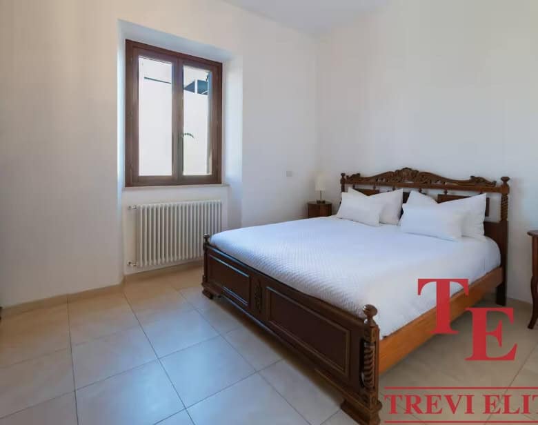 Elegant bedroom with antique wooden bed, large window with wooden frame, and minimalist decor in a luxurious Italian property.