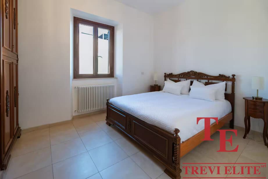 Elegant bedroom with antique wooden bed, large window with wooden frame, and minimalist decor in a luxurious Italian property.