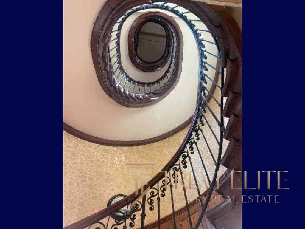 Spiral staircase view from the top, showcasing elegant wooden steps and ornate black wrought iron railing in a luxurious Italian property. Perfect for high-end real estate listings.