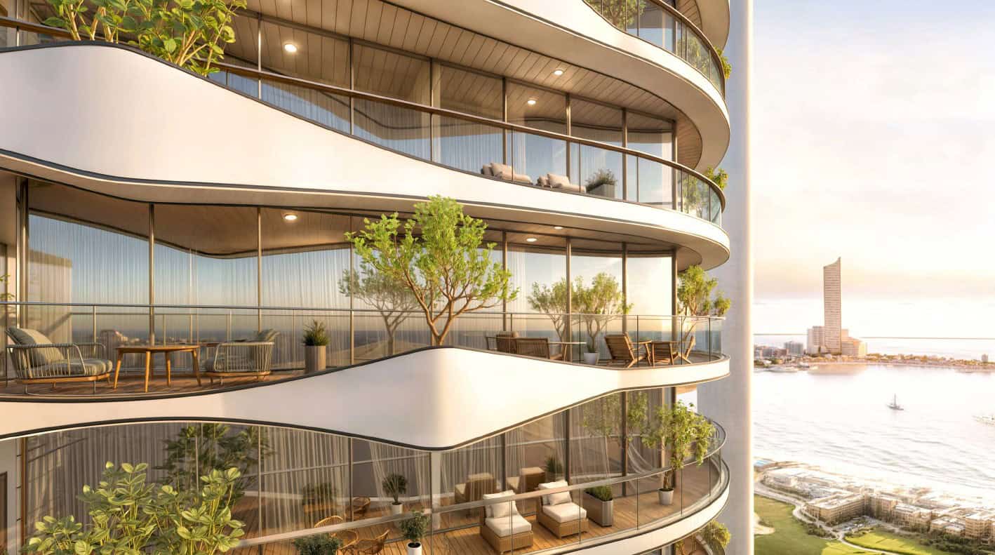Luxurious modern apartment building with spacious curved glass balconies overlooking the water at sunset, featuring outdoor seating and lush greenery.