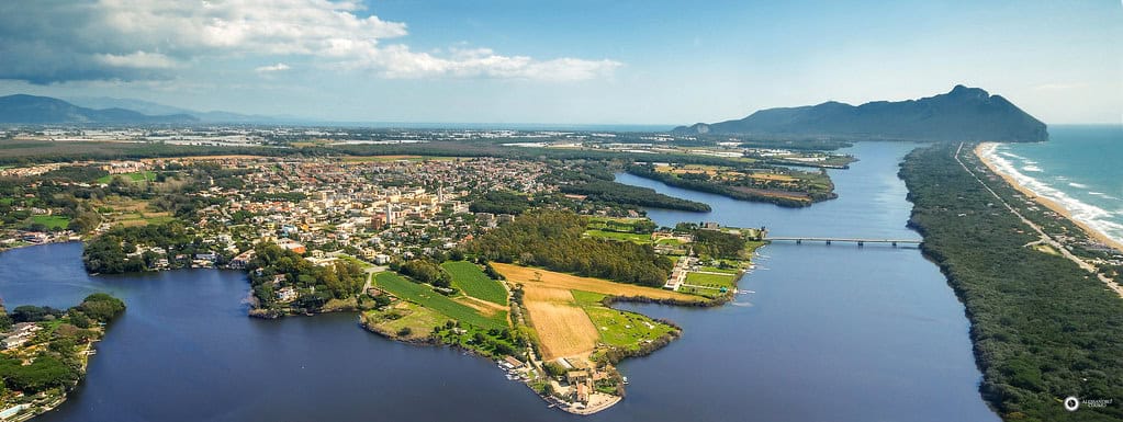 Lush green landscape with lakes, a town, and coastal mountains in Italy, showcasing scenic natural beauty and luxurious living options by the water.