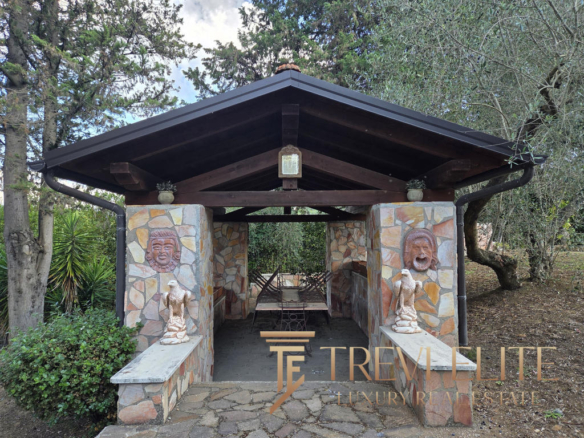 Charming outdoor stone gazebo with decorative masks and lush greenery, perfect for relaxed gatherings in scenic Italian countryside.