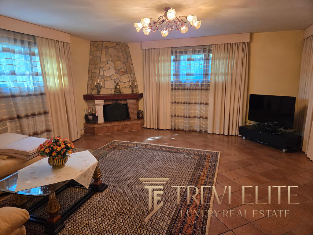 Luxurious living room with stone fireplace, elegant curtains, plush seating, and a flat-screen TV, showcasing sophisticated Italian interior design and high-end features at Trevi Elite.