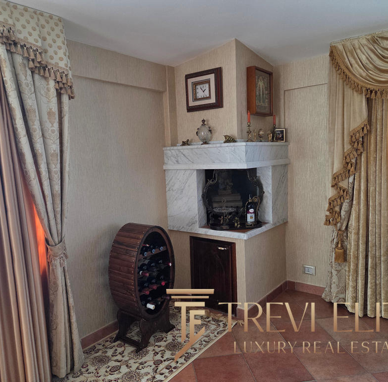 Lavishly decorated corner featuring a marble fireplace with vintage ornaments; elegant drapes adorn the windows, complemented by a personalised wine rack with red, white, and rosé bottles.