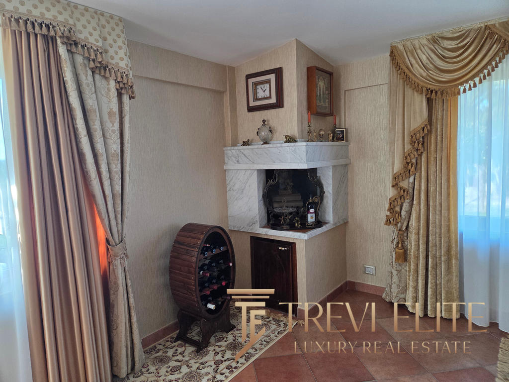 Lavishly decorated corner featuring a marble fireplace with vintage ornaments; elegant drapes adorn the windows, complemented by a personalised wine rack with red, white, and rosé bottles.