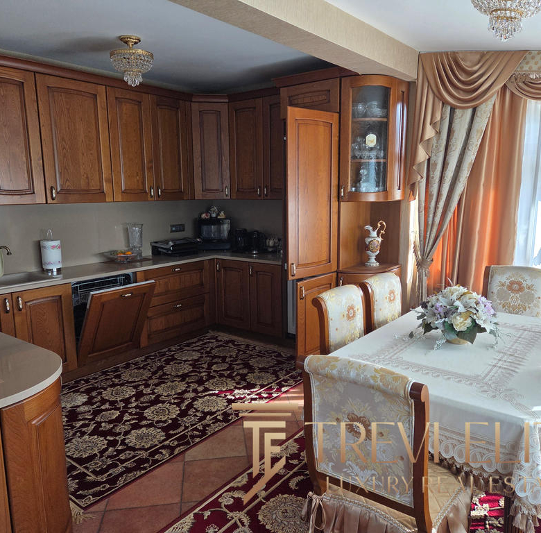 A cosy, classic kitchen and dining area with wooden cabinetry, elegant curtains, and a floral tablecloth, showcasing timeless Italian interior design and craftsmanship in a luxurious property.