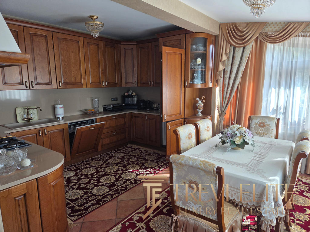 A cosy, classic kitchen and dining area with wooden cabinetry, elegant curtains, and a floral tablecloth, showcasing timeless Italian interior design and craftsmanship in a luxurious property.