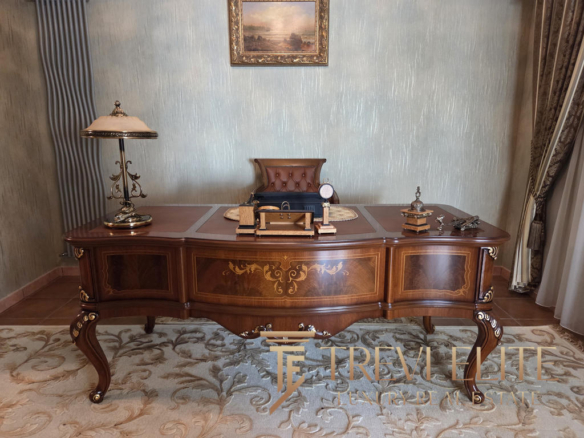 Elegant antique wooden desk with ornate gold detailing in an opulent office setting.