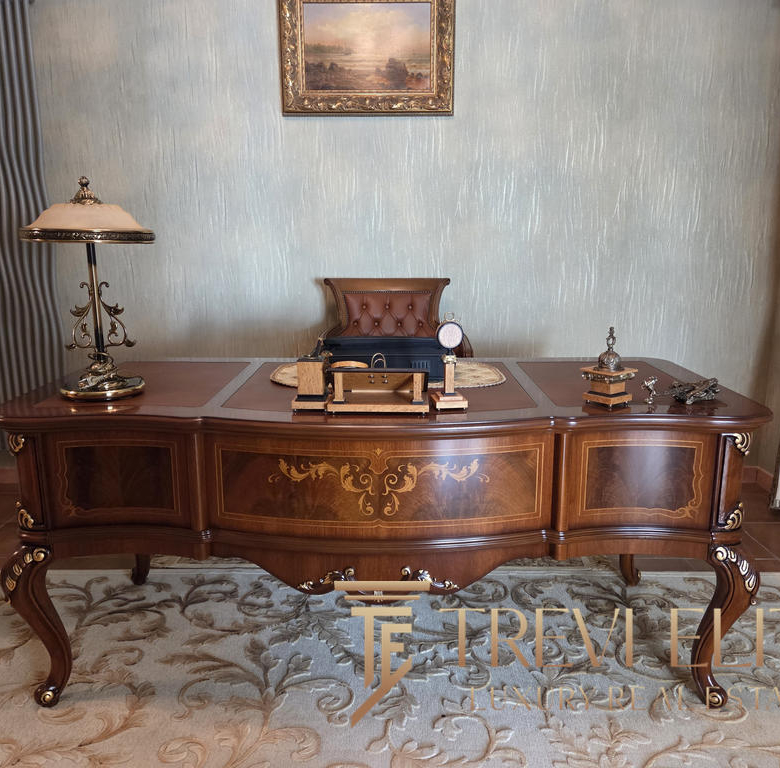 Elegant antique wooden desk with ornate gold detailing in an opulent office setting.