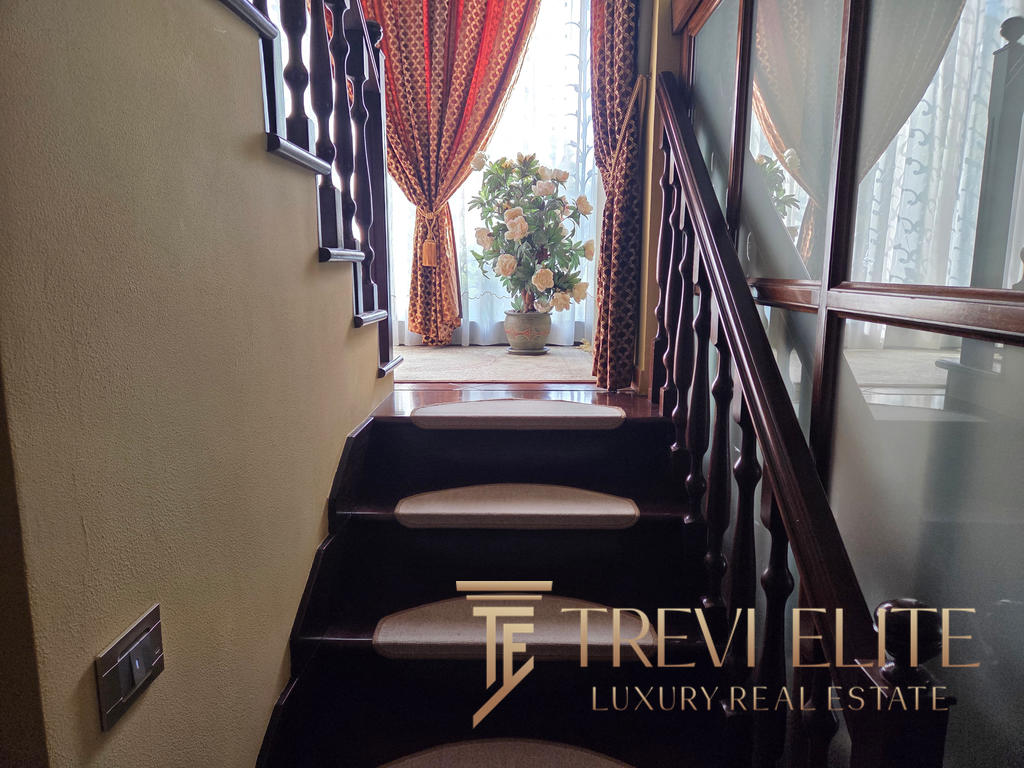 Elegant staircase leading to a sunlit room with lush floral decor and luxurious curtains, showcasing the sophisticated Italian real estate offerings by Trevi Elite.